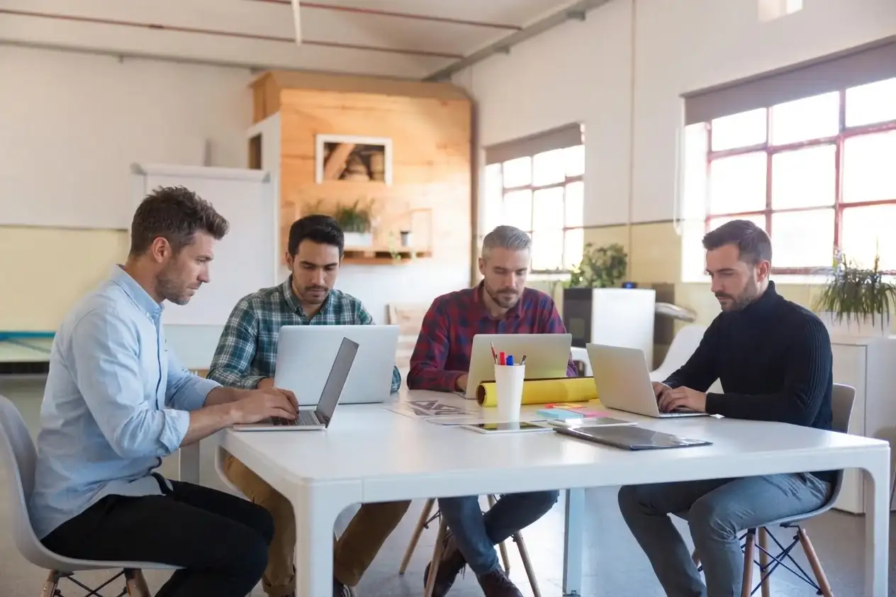 A group of four men at a table, focused on their laptops, likely working together on a project.