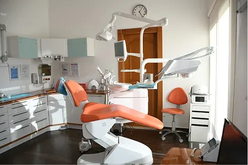 Modern dental clinic treatment room featuring an ergonomic orange patient chair and advanced overhead medical equipment for a professional dental practice overview.